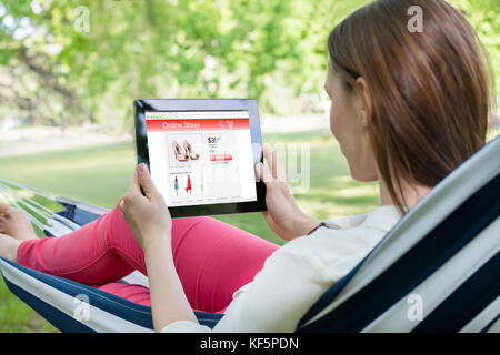 Young Woman Lying In Hammock Shopping Online With Digital Tablet Stock Photo