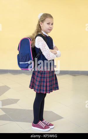 Fird class schoolgirl with backpack standing in school hall, full length portrait Stock Photo