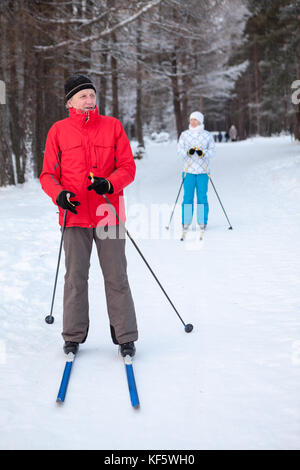 Mature male skier and woman stay on skis in winter snow skiing run Stock Photo