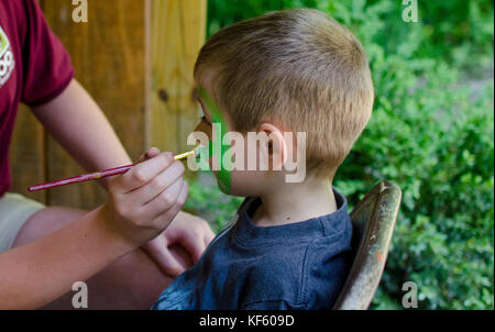 A boy with green face paint being painted Stock Photo