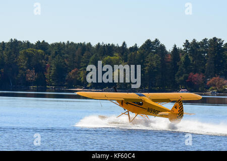 Bright yellow 2005 Cub Crafters float plane taking off on Lake Pleasant in the Adirondack Park. Stock Photo