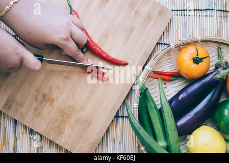 close up woman cutting chili on a cutting board with vegetables beside.home concept Stock Photo