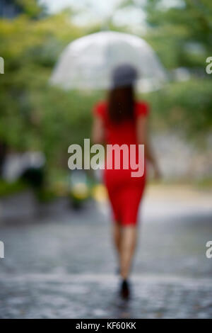 License and prints at MaximImages.com - Woman in red elegant dress walking with an umbrella in the rain on a city street