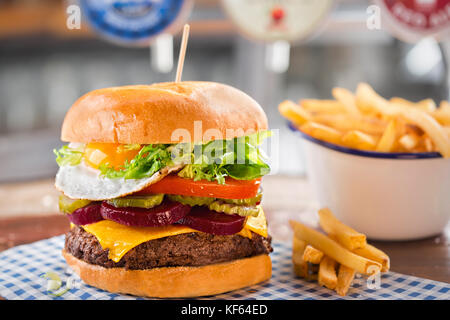 Beef burger with cheese, lettuce, tomato, beetroot & pickle, topped with a fried egg Stock Photo