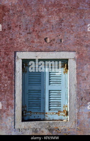 Some painted shutters on a window of an old derelict house in greece. Shabby chic styling and peeling distressed paintwork rural or rustic styles. Stock Photo