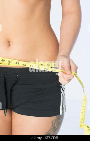 Close up of a young woman measuring her waist with a tape measure Stock Photo