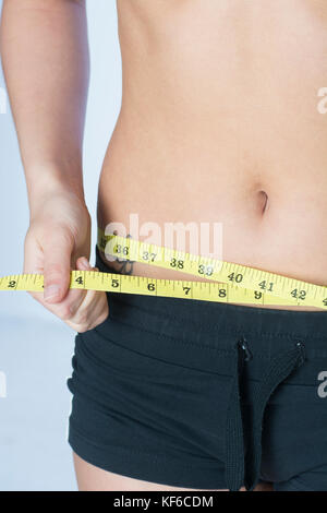 Close up of a young woman measuring her waist with a tape measure Stock Photo
