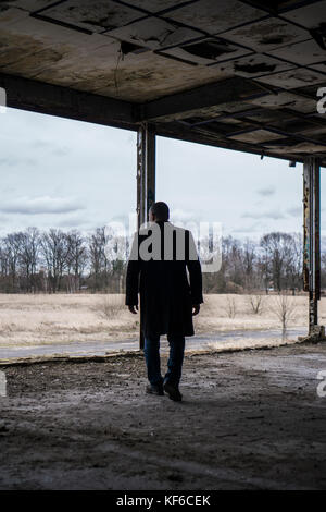 Rear view of a man wearing a coat walking inside a derelict building Stock Photo