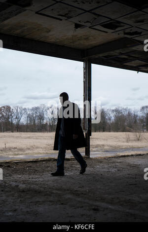 Side view of a man wearing a coat walking inside a derelict building Stock Photo