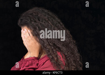 Portrait of a young woman hiding face with hands against a black background Stock Photo