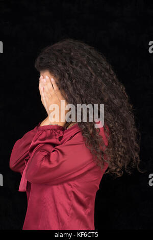 Portrait of a young woman hiding face with hands against a black background Stock Photo