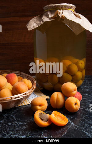 Ripe organic apricots harvested at summer time and big glass jar with canned sweet apricot compote on dark marble. Composition in rustic style - organ Stock Photo