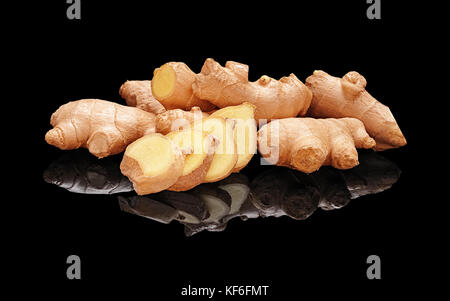Pile fresh not peeled ginger roots with slices isolated on black glossy background with real reflection. Side view Stock Photo