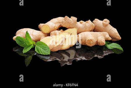 Pile fresh not peeled ginger roots with slices and mint leaf isolated on black glossy background with real reflection. Side view Stock Photo
