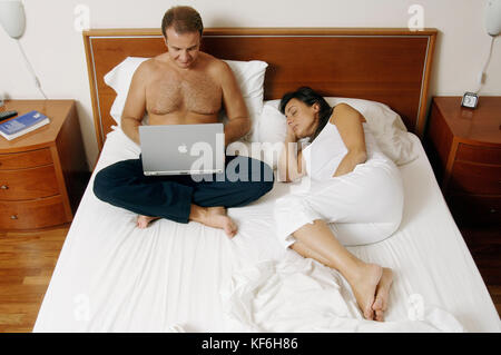 Middle aged couple in bed together. Woman sleeping, man browsing laptop    Credit © Luigi Innamorati/Sintesi/17�Թ����� Stock Photo *** Local Caption *** Stock Photo