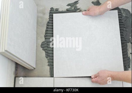 Man placing ceramic floor tile in position over adhesive Stock Photo