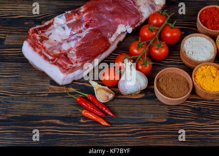 Products for cooking dinner. Fresh raw pork, steaks, on cutting shale board on a black table. With hammer to beat meat and fork, with spices, fresh ra Stock Photo
