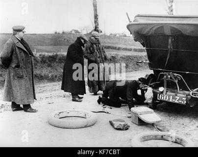 Alfred Harmsworth, Lord Northcliffe in fur coat, watches as chauffeur changes wheel on 1908 Mercedes Stock Photo