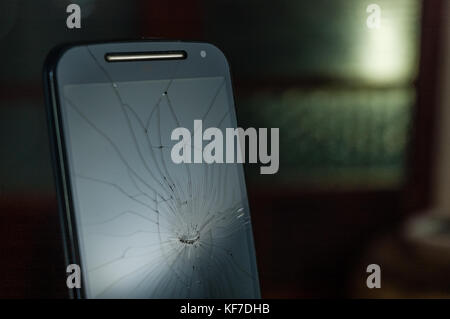 Top half of broken black smartphone with cracked screen lit against a dark background Stock Photo