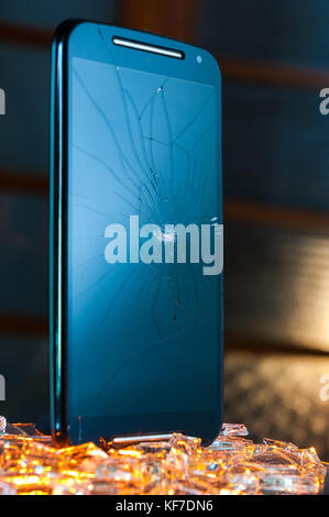 Broken black smartphone with cracked screen standing vertically on pieces of broken glass Stock Photo