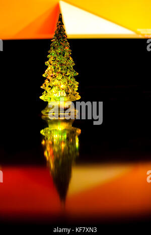 A small lighting Christmas tree on the contrast dark and orange geometric background. Selective focus, reflections, geometric lines. Abstract colorful Stock Photo