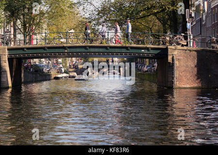 View from the water level of a canal in a bustling city, with people gathering on an arching bridge. Stock Photo
