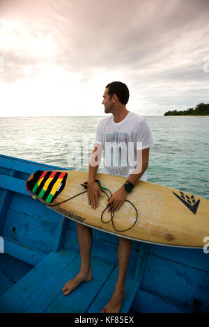INDONESIA, Mentawai Islands, Kandui Surf Resort, young man sitting on boat with surfboard Stock Photo