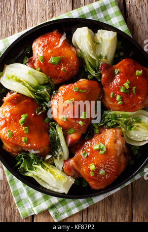 Fried chicken thighs with bok choy and green onions close-up on a plate. Vertical top view from above Stock Photo