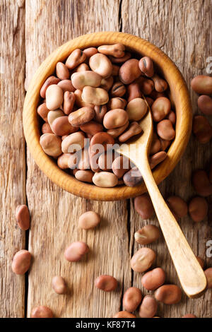 Organic dried broad beans close-up in a wooden bowl on a table. Vertical top view from above Stock Photo