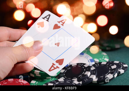 Casino chips and pair of aces in a croupier's hand against bright bokeh lights. Poker game theme concept. Stock Photo