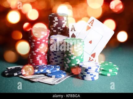 Casino chips and cards, two aces on the playing green table against bright bokeh lights. Poker game theme backdrop Stock Photo