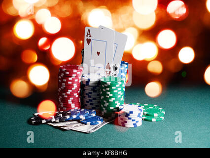 Casino chips and cards, two aces on the playing green table against bright bokeh lights. Poker game theme backdrop Stock Photo