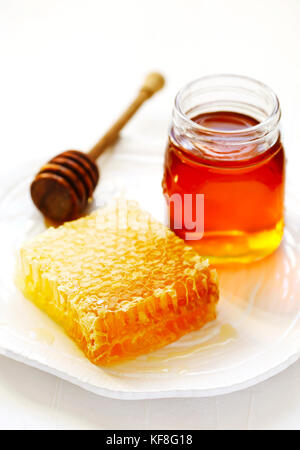 Honeycombs with honey, honey in glass jar and wooden honey dipper on plate Stock Photo
