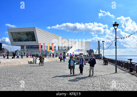 Liverpool Pier Head waterfront 3 M/R tourists nearest camera strolling along the promenade beside River Mersey with the Museum of Liverpool beyond UK Stock Photo