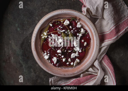 Vegetarian beetroot carpaccio salad with feta cheese, thyme, olive oil and capers in terracotta plate on textile napkin over old metal background. Top Stock Photo