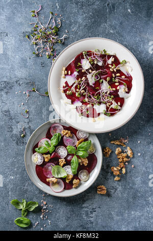 Vegetarian beetroot carpaccio salads with radish, basil, olive oil, goat cheese, walnuts, pine and sprouts in two plate over blue texture background.  Stock Photo