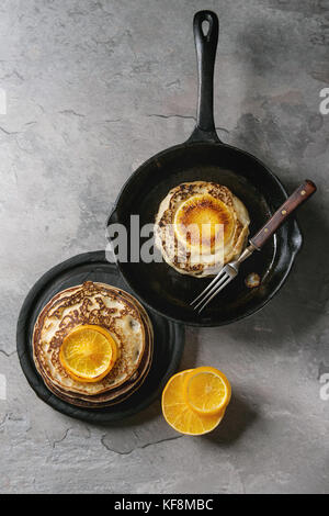 Homemade pancakes with fried orange, served in cast-iron pan and black plate on gray texture background. Top view with space Stock Photo