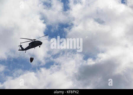 Black Hawk helicopter with hanging water bucket flying over forest fire on Dilly Cliff in Kinsman Notch, New Hampshire in October 2017. These cliffs a Stock Photo