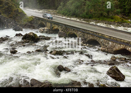 Pickup truck driving on old stone bridge crossing river rapids. Stock Photo