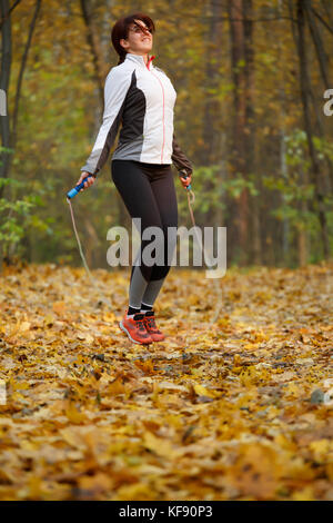 Side view of sporty woman jumping with rope at autumn forest Stock Photo