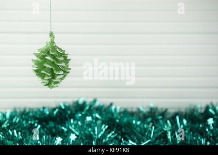 Christmas photography picture of xmas tree decoration hanging up of green pine cone with snow glitter and colored tinsel and white wood background Stock Photo