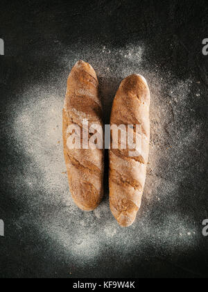 Two whole homemade buckwheat loaf bread with buckwheat flour on black textured background. Top view or flat-lay. Low key Stock Photo