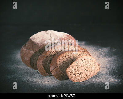 Sliced homemade sourdough rye bread with rye flour on black textured background. Copy space. Low key Toned image Stock Photo