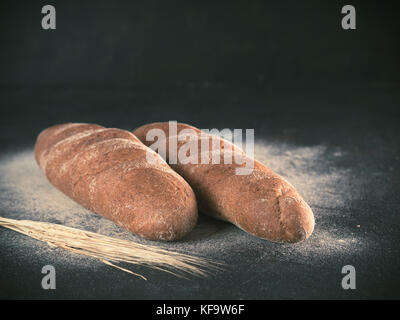 Two whole homemade rye loaf bread with buckwheat flour on black textured background. Copy space. Low key Toned image Stock Photo