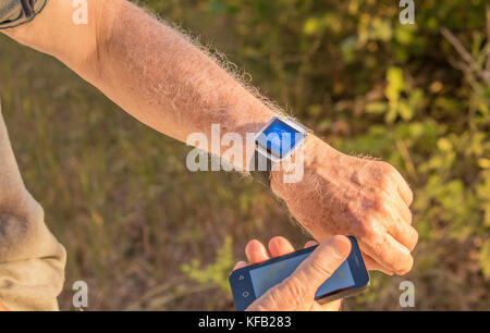 Senior man checking his fitness information using his smart device and phone; grass in the background Stock Photo