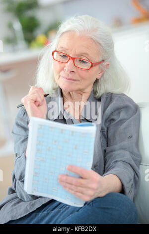 pensioner wearing reading glasses doing magazine puzzle Stock Photo