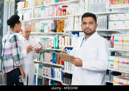 Chemist Holding Clipboard While Colleague And Customer Standing  Stock Photo