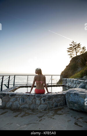 USA, California, Big Sur, Esalen, a woman sits on the edge of the hot spring at the Baths and takes in the evening view, the Esalen Institute Stock Photo