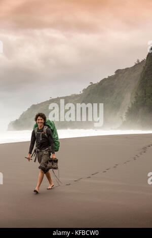 USA, Hawaii, The Big Island, backpacker walks on the beach along the surf in the Waipio Valley Stock Photo