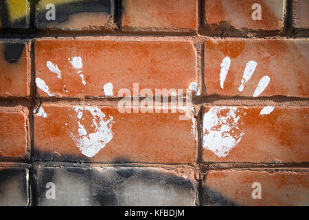 White paint prints of two hands on colourful graffity on a brick wall Stock Photo